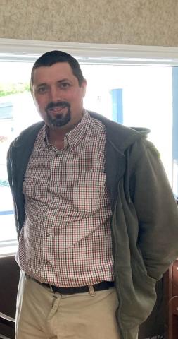 A man wearing a grey sweater over a plaid buttoned shirt and khakis