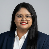 Girl with long black hair. She is wearing brown framed glasses, a black blazer over a white button up shirt