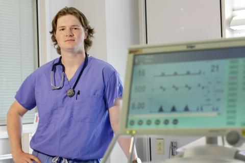 Man with blonde hair wearing blue scrubs with a hospital machine